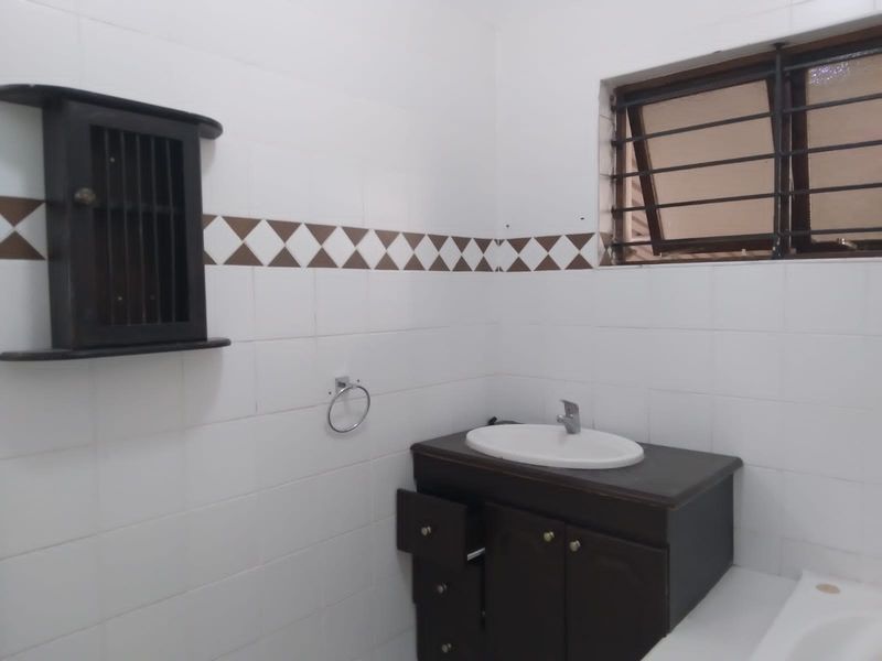 A functional bathroom featuring a vanity cabinet with basin, tiled walls, and a window with security bars, requiring minor cosmetic updates.