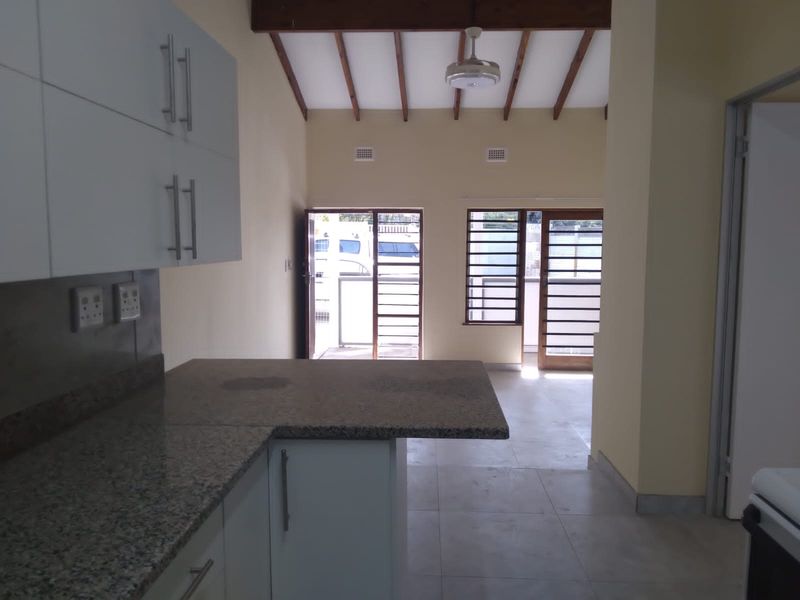 Open plan kitchen and living area featuring granite countertops, modern cabinetry, exposed timber ceiling beams, and tiled flooring with access to the exterior.