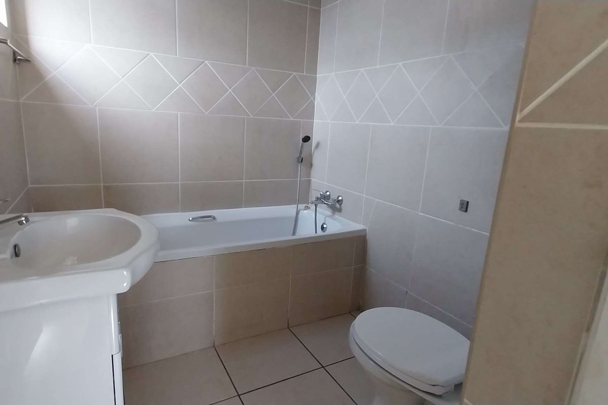 A functional bathroom featuring a pedestal basin, a standard bathtub with shower mixer, and a toilet, finished with neutral ceramic wall and floor tiles.