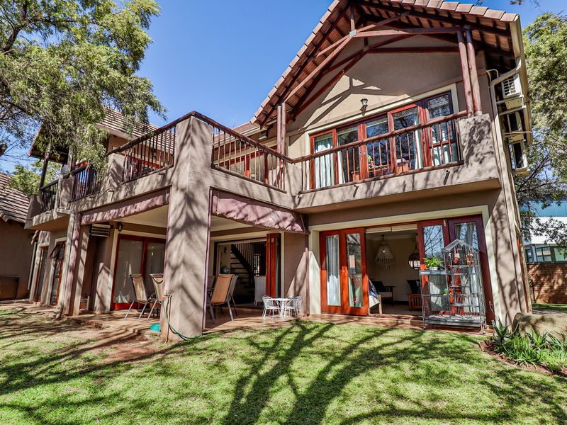 Rear view of a double-story residence featuring a covered patio, upper-level balcony with timber railings, and large timber-framed glass doors opening to the garden.