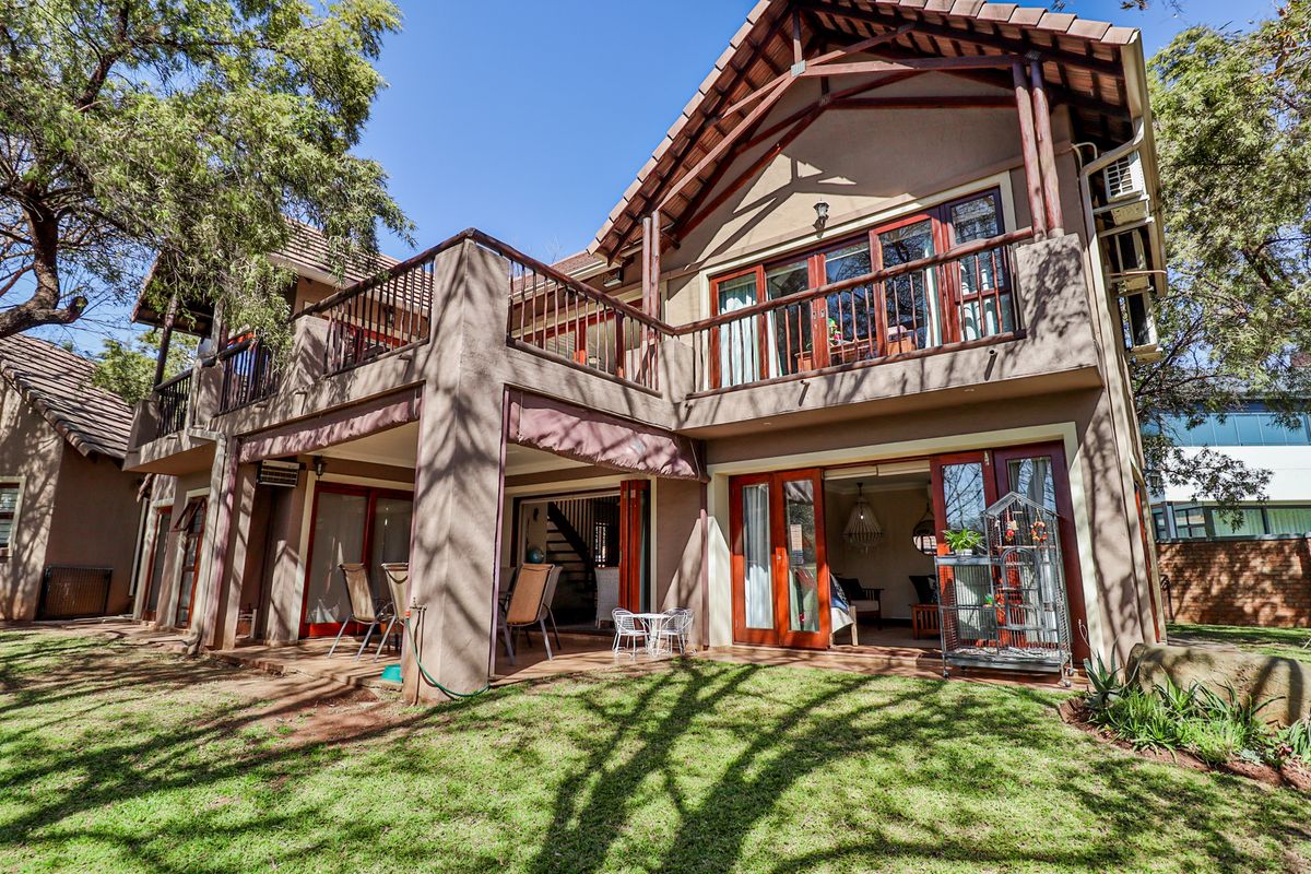 Rear view of a double-story residence featuring a covered patio, upper-level balcony with timber railings, and large timber-framed glass doors opening to the garden.