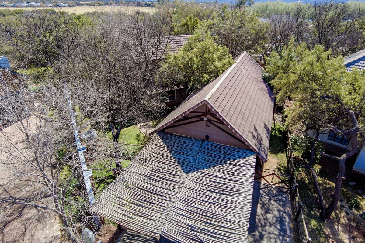 Aerial view of the property featuring a tiled roof structure, a large pergola, and surrounding landscaped garden area with mountain views.
