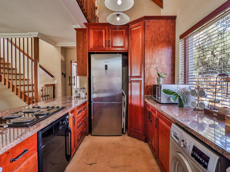 A functional kitchen featuring warm wooden cabinetry, granite countertops, built-in oven, and hob, with an adjacent staircase and integrated laundry space.