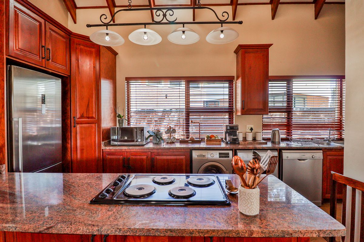 A well-appointed kitchen featuring rich wooden cabinetry, granite countertops, a central hob, and integrated appliances including a washing machine and dishwasher.