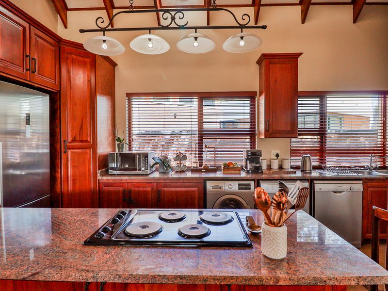 A well-appointed kitchen featuring rich wooden cabinetry, granite countertops, a central hob, and integrated appliances including a washing machine and dishwasher.