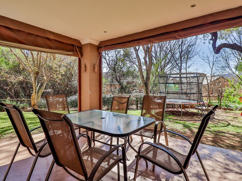 A covered outdoor patio area featuring concrete flooring and recessed lighting, overlooking a private garden space.