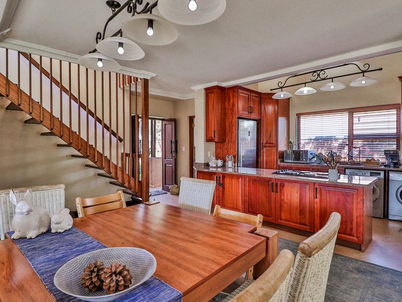 Open-plan kitchen and dining area featuring warm-toned wooden cabinetry, granite countertops, and an adjacent wooden staircase leading to the upper level.