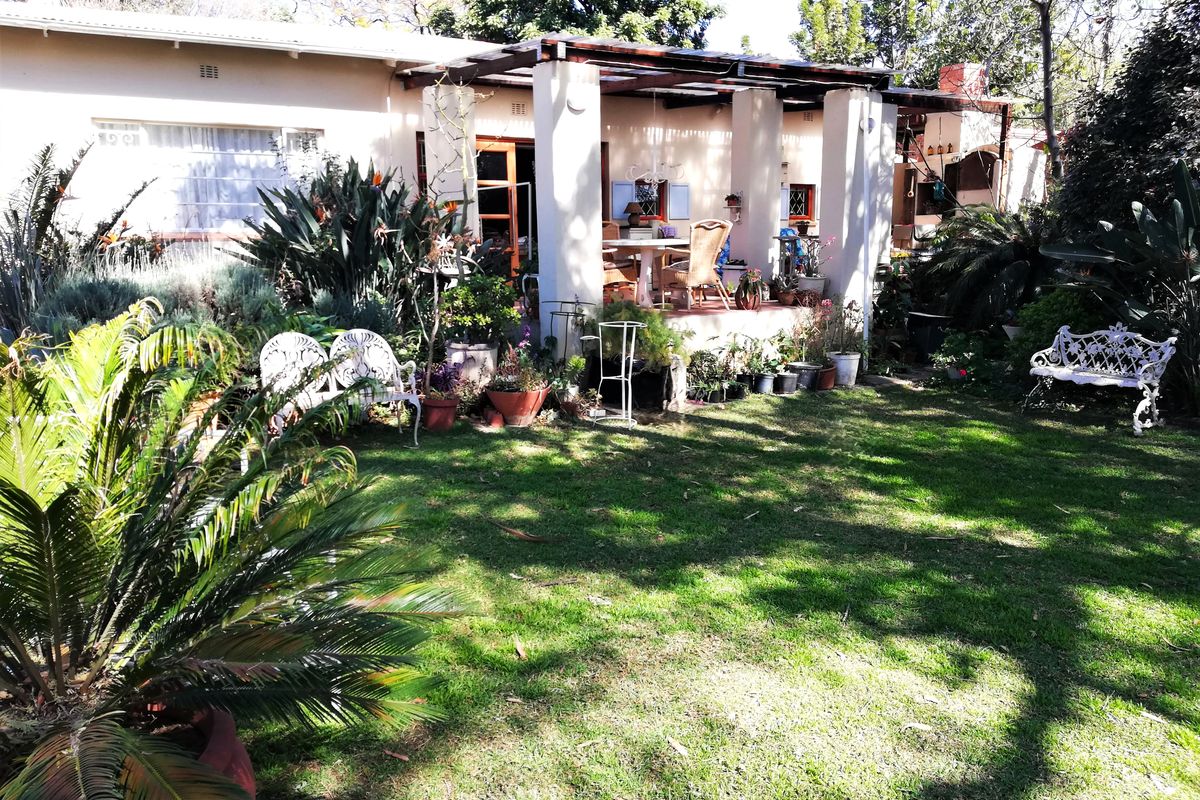 A rear view of the house featuring a covered patio area overlooking a well-established garden with a lawn.