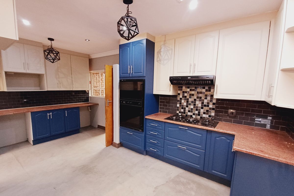 A spacious kitchen featuring a mix of blue and cream cabinetry, built-in oven, gas hob, extractor fan, and dark tiled backsplashes.