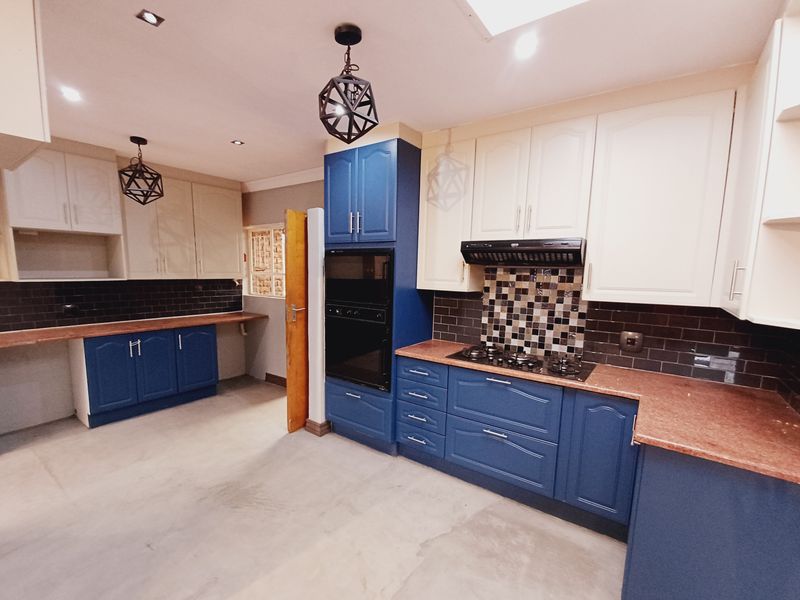 A spacious kitchen featuring a mix of blue and cream cabinetry, built-in oven, gas hob, extractor fan, and dark tiled backsplashes.