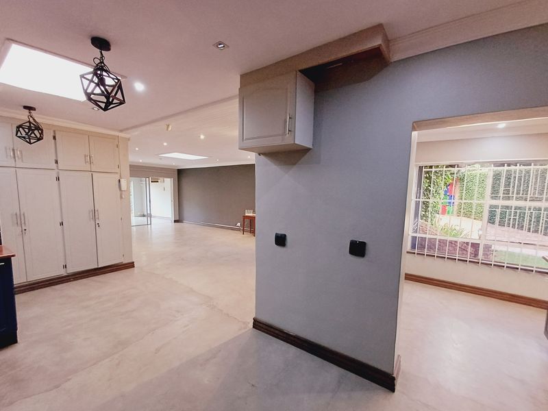 Spacious open-plan living area featuring neutral flooring, built-in storage cabinetry, recessed lighting, and large windows with security bars, offering a bright and versatile layout.