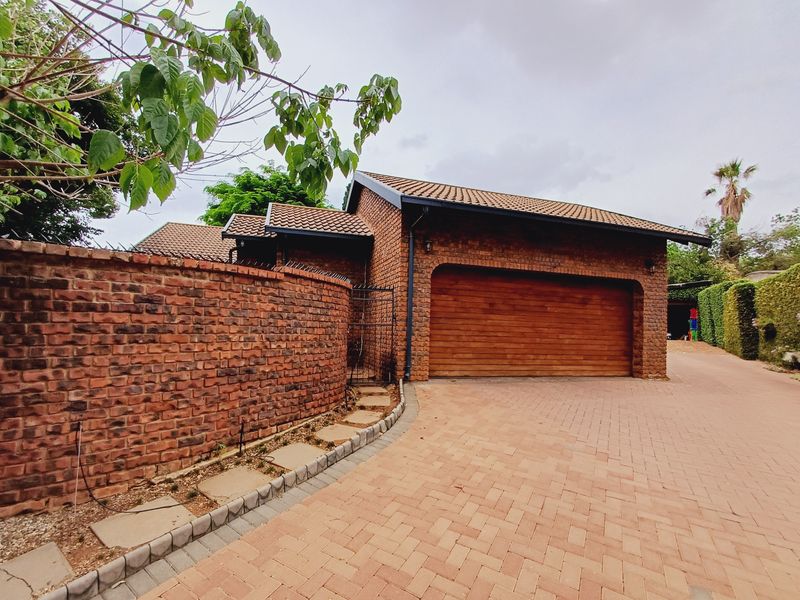 Front exterior view of the property featuring a face brick facade, double garage, and paved driveway with a secure boundary wall.