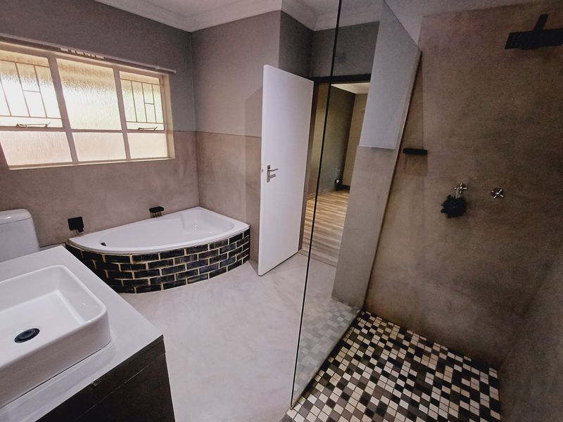 Modern bathroom featuring a walk-in shower with glass screen, a vessel sink vanity, and a unique brick-clad built-in bathtub.