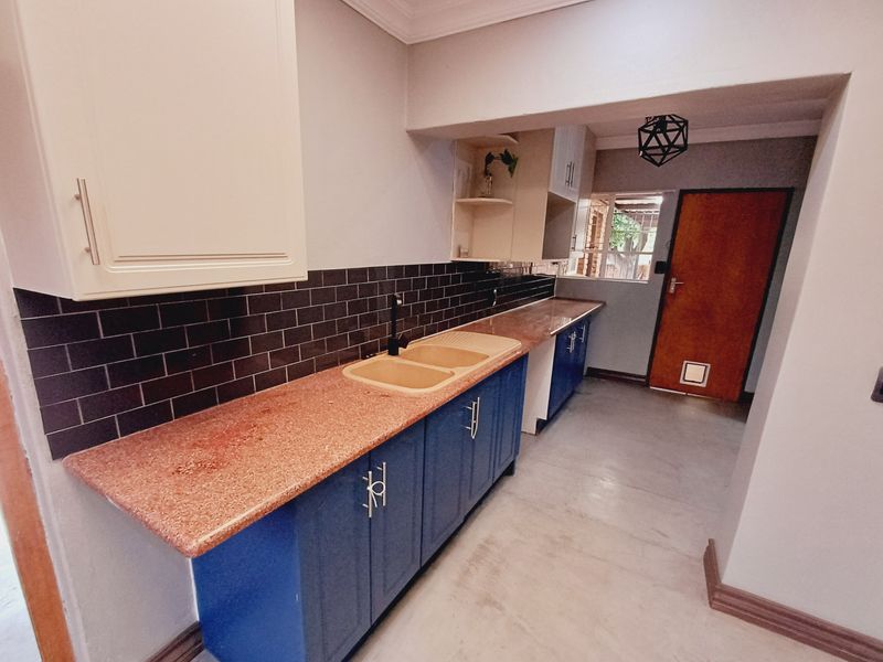 A functional scullery area featuring blue base cabinetry, stone countertops, a double sink, and a subway tile backsplash with direct access to the exterior.