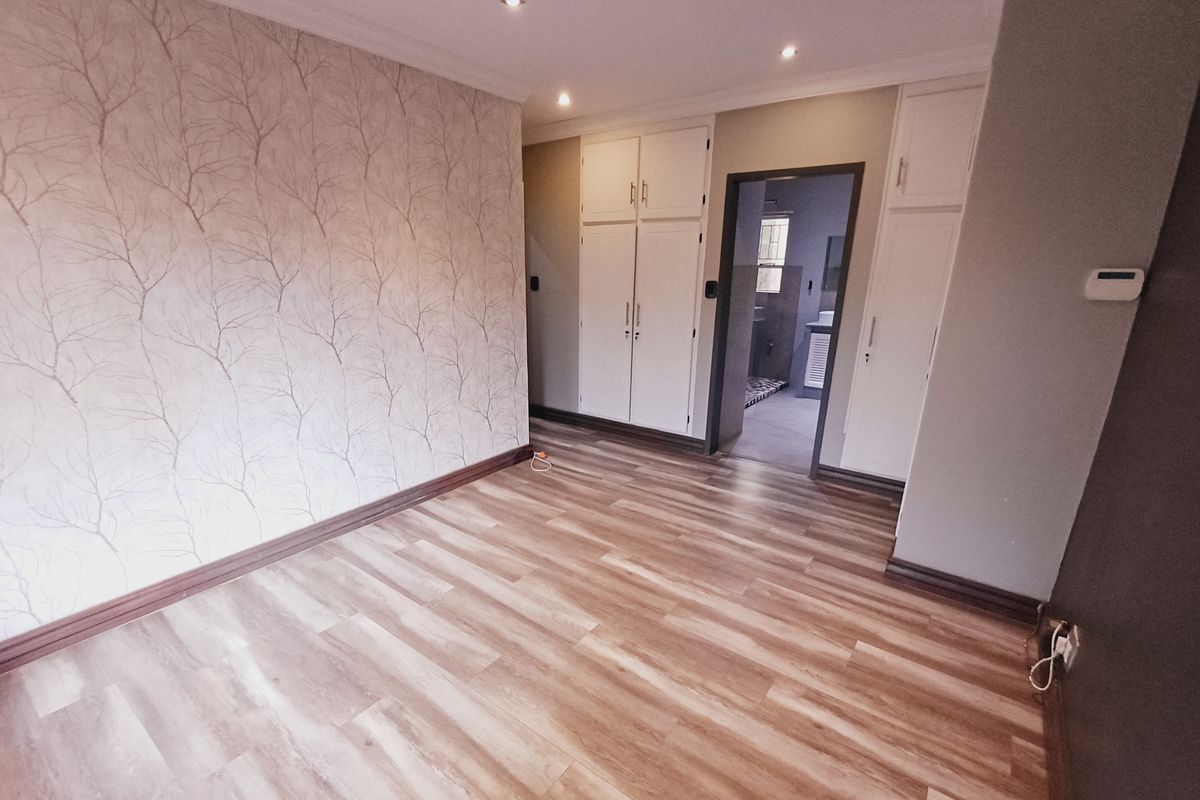 Spacious bedroom featuring modern laminate flooring, built-in cupboards, and recessed lighting, with an adjoining bathroom visible through the doorway.
