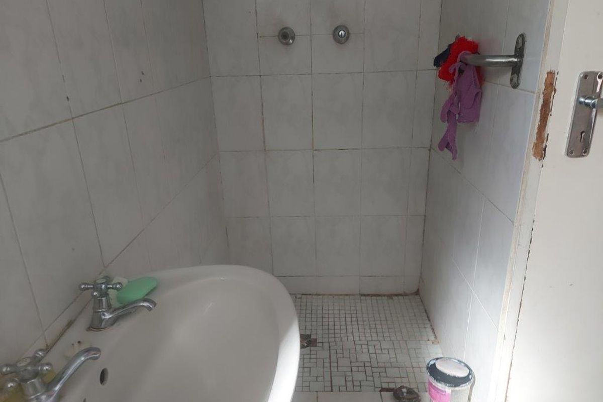 A compact bathroom featuring a pedestal basin and shower area with tiled finishes, requiring maintenance to the door frame and tile surfaces.