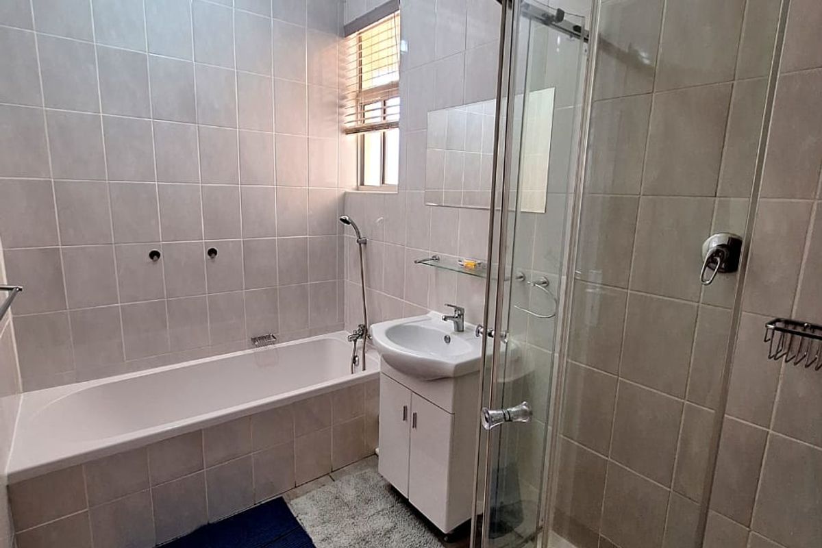 A functional bathroom featuring a separate bathtub, a glass-enclosed corner shower, and a vanity basin with tiled walls and flooring.