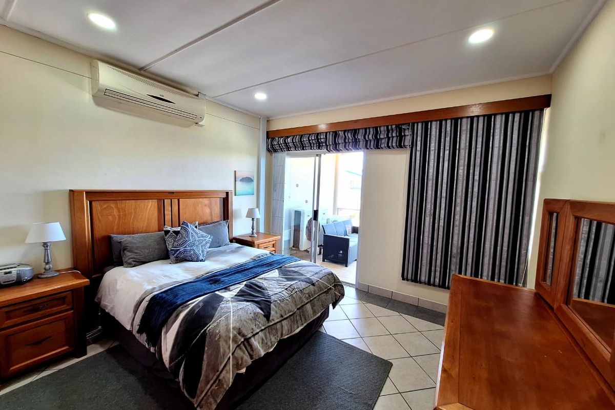 Spacious bedroom featuring tiled flooring, recessed lighting, a wall-mounted air conditioning unit, and direct access to a private balcony through sliding glass doors.
