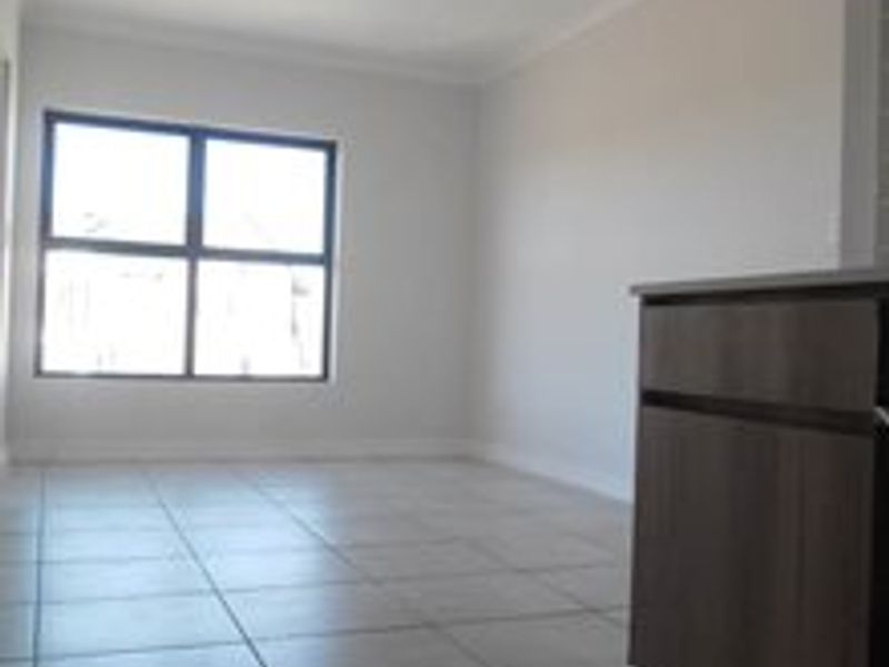 An empty open-plan living and kitchen area featuring neutral tiled flooring, built-in cabinetry, and a large window providing natural light.