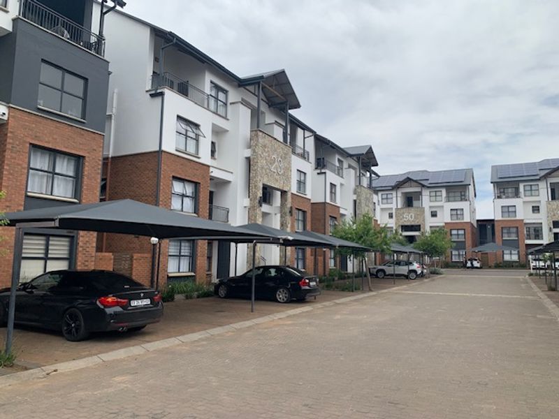 Exterior view of a modern apartment complex featuring brick and plaster facades, private balconies, and covered parking bays.