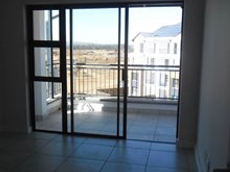 An empty living area featuring tiled flooring and large sliding glass doors that open onto a private balcony with exterior views.