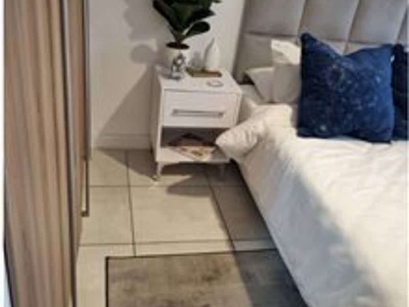 A well-maintained bedroom featuring neutral tiled flooring and a modern built-in wardrobe with wood-grain finish.
