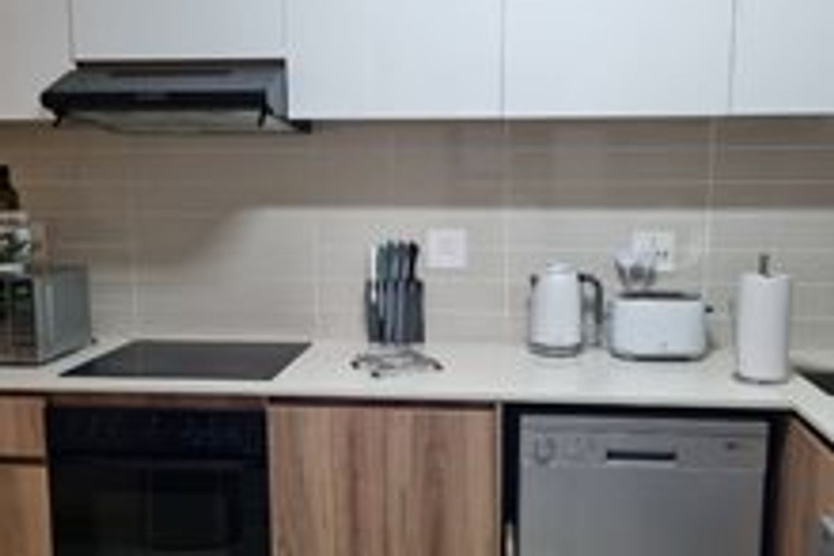 Modern kitchen featuring sleek white upper cabinetry, wood-finish lower cabinets, stone countertops, and integrated appliances including an oven, hob, and dishwasher.