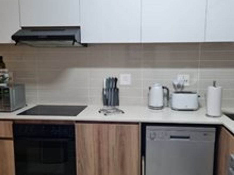 Modern kitchen featuring sleek white upper cabinetry, wood-finish lower cabinets, stone countertops, and integrated appliances including an oven, hob, and dishwasher.