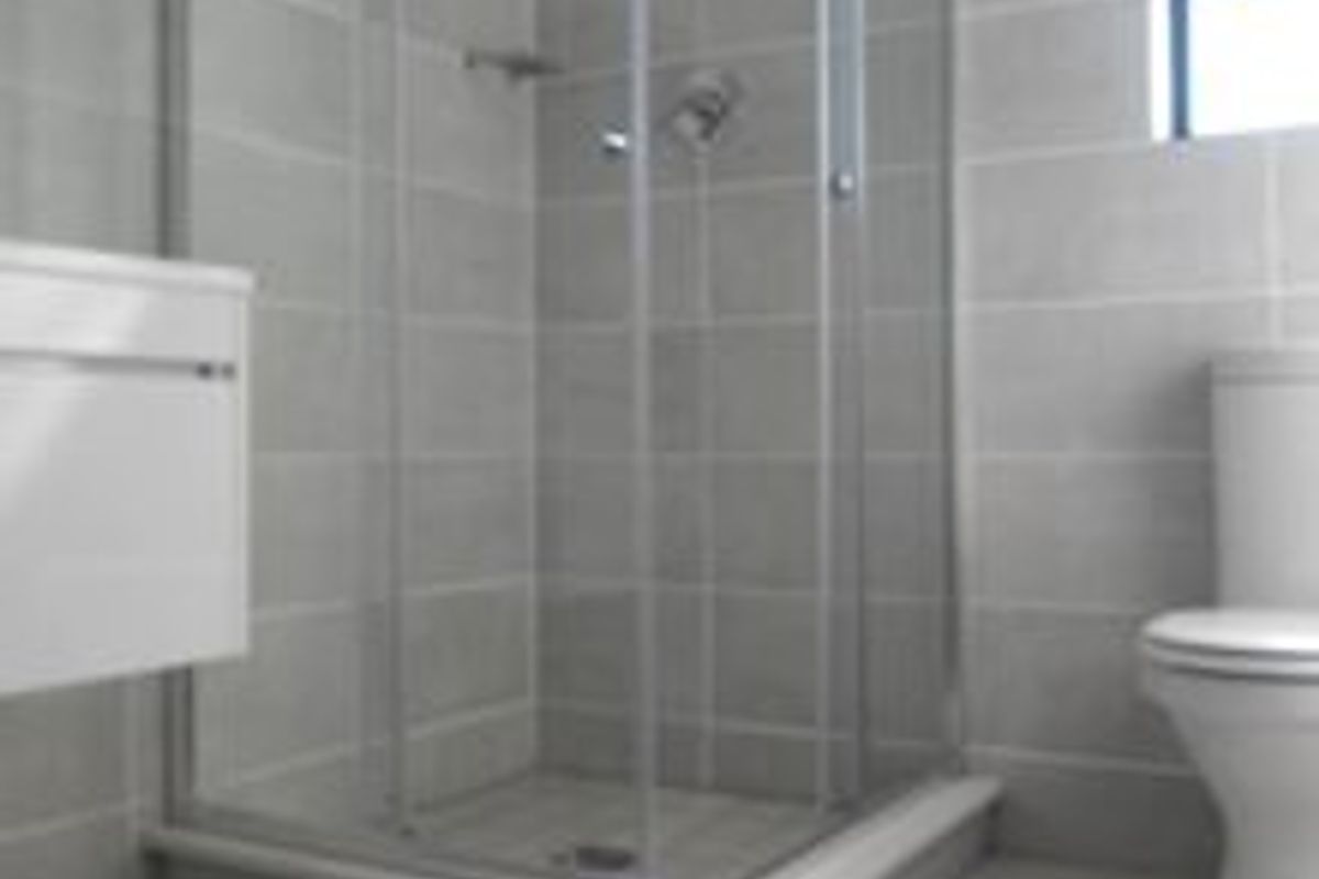 A clean, modern bathroom featuring a glass shower enclosure, wall-mounted vanity, and neutral grey floor-to-ceiling tiling.