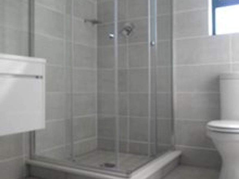A clean, modern bathroom featuring a glass shower enclosure, wall-mounted vanity, and neutral grey floor-to-ceiling tiling.