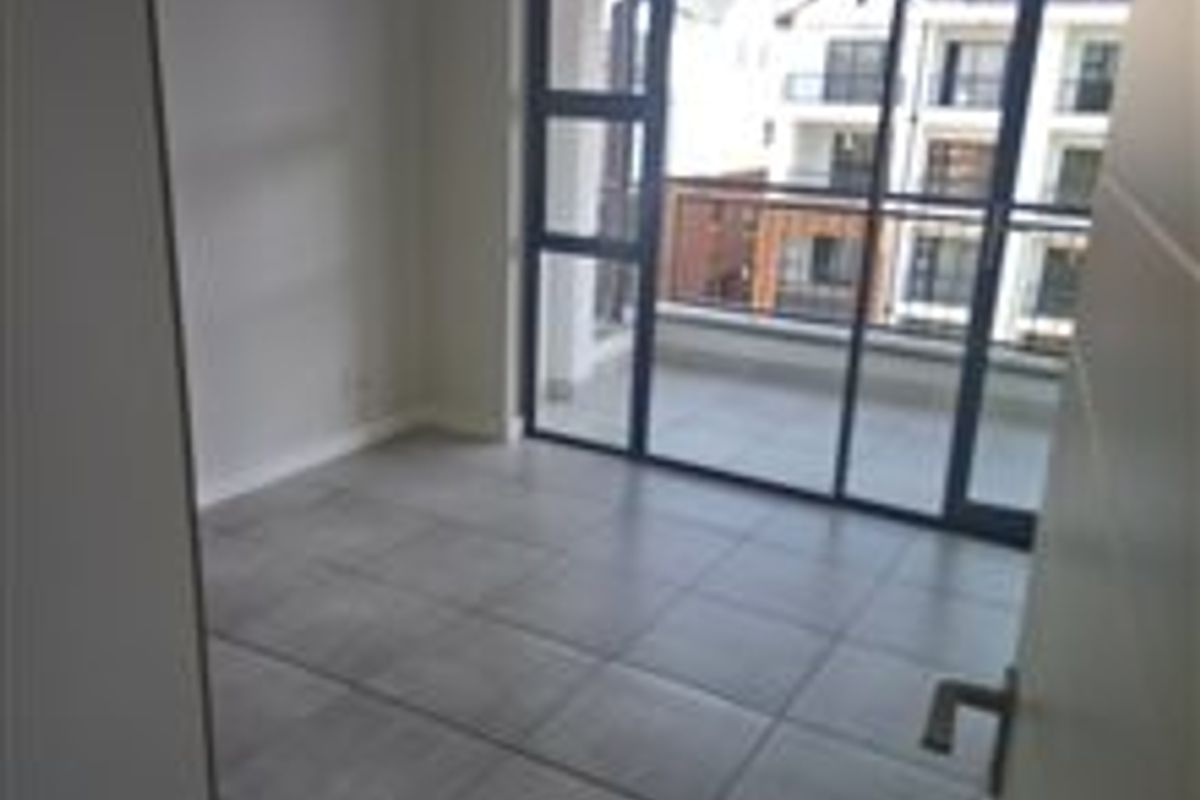 A bright, empty bedroom featuring large format floor tiles and a sliding glass door providing access to an outdoor balcony.