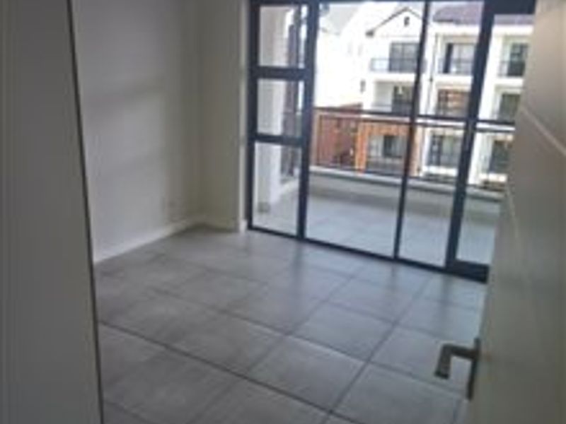 A bright, empty bedroom featuring large format floor tiles and a sliding glass door providing access to an outdoor balcony.