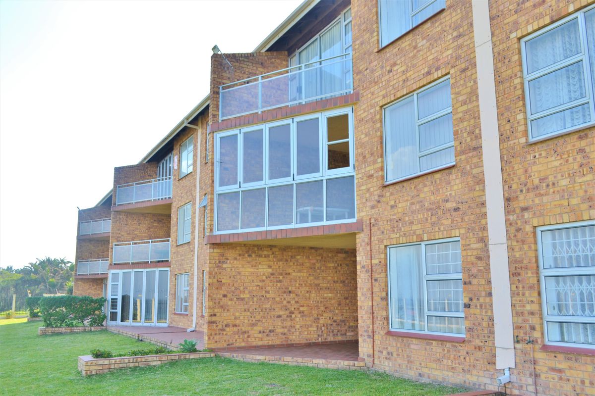 Exterior view of a multi-story apartment building featuring face-brick facade, glass-enclosed balconies, and aluminum-framed windows overlooking a communal garden area.