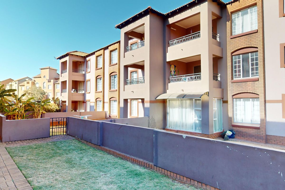 Rear view of a multi-story townhouse complex featuring private balconies, brick facade detailing, and a small enclosed garden area with paved pathways.