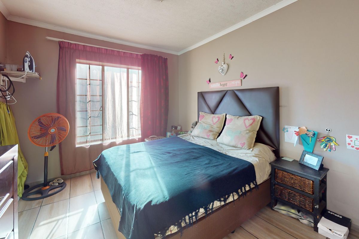 A standard bedroom featuring tiled flooring, a window with security bars, and built-in cupboard storage.