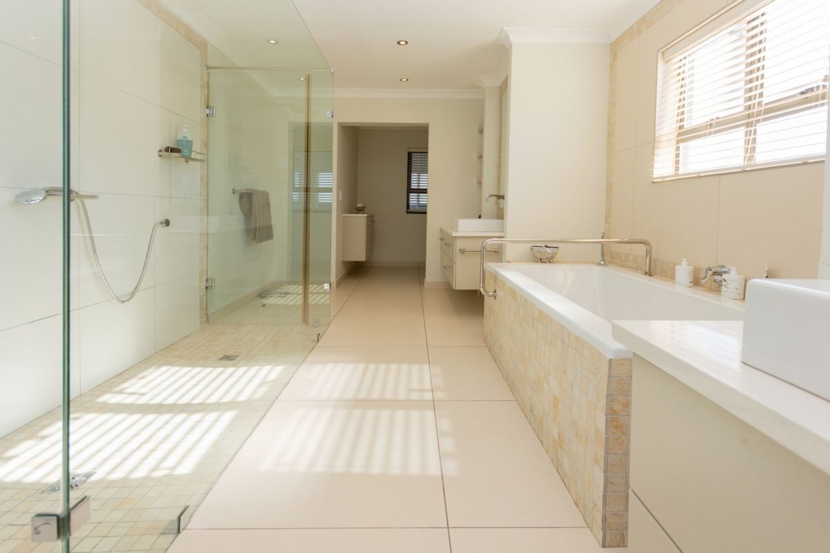 Spacious modern bathroom featuring a large glass-enclosed shower, built-in bathtub with mosaic tile detailing, and a sleek vanity unit.