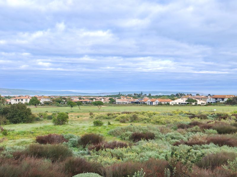 A scenic landscape view overlooking a golf course and surrounding residential estate under a cloudy sky.