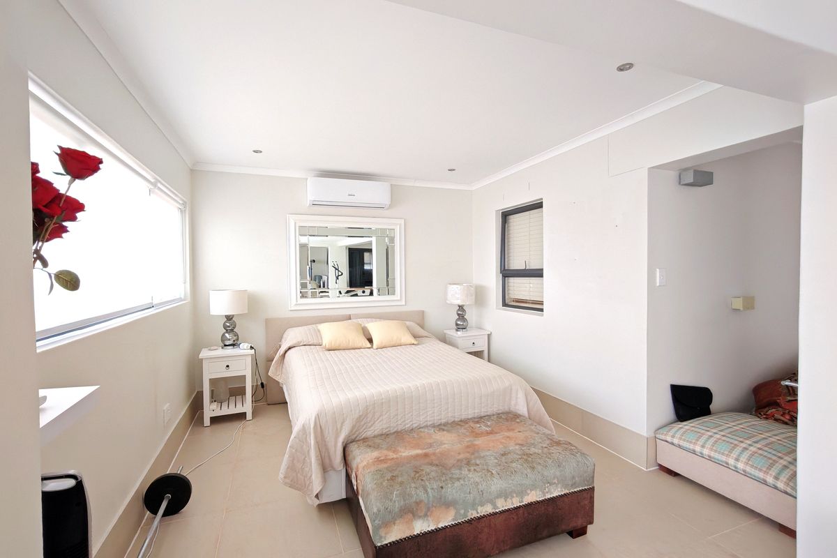 A well-lit bedroom featuring tiled flooring, recessed downlighting, and a wall-mounted split-system air conditioning unit.