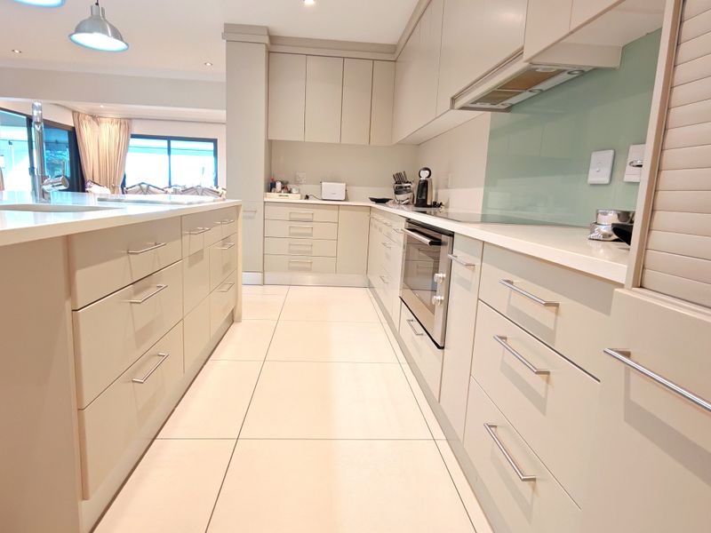 Modern kitchen featuring sleek built-in cabinetry, stone countertops, a central island, integrated oven, and high-quality tiled flooring with recessed lighting.
