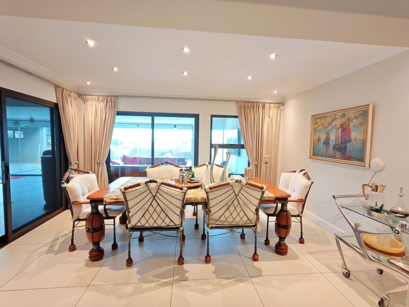A bright dining room featuring large sliding glass doors that open to an outdoor area, complemented by neutral tiled flooring and recessed downlighting.