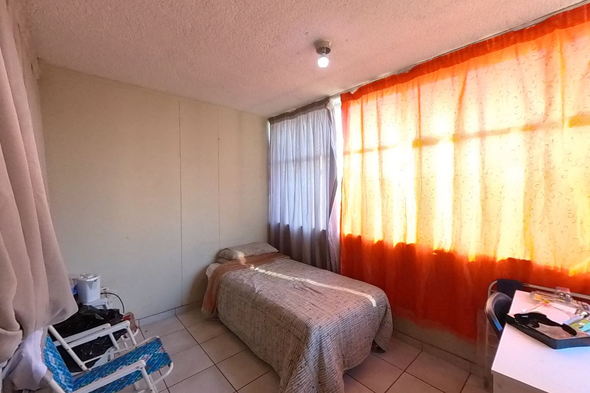 A bedroom featuring tiled flooring and a large window, providing natural light. The space requires cosmetic updates to improve its overall condition.