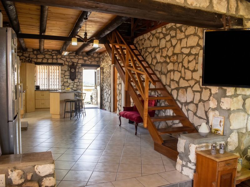 Open plan living area featuring rustic stone walls, exposed timber ceiling beams, and a wooden staircase leading to an upper level.