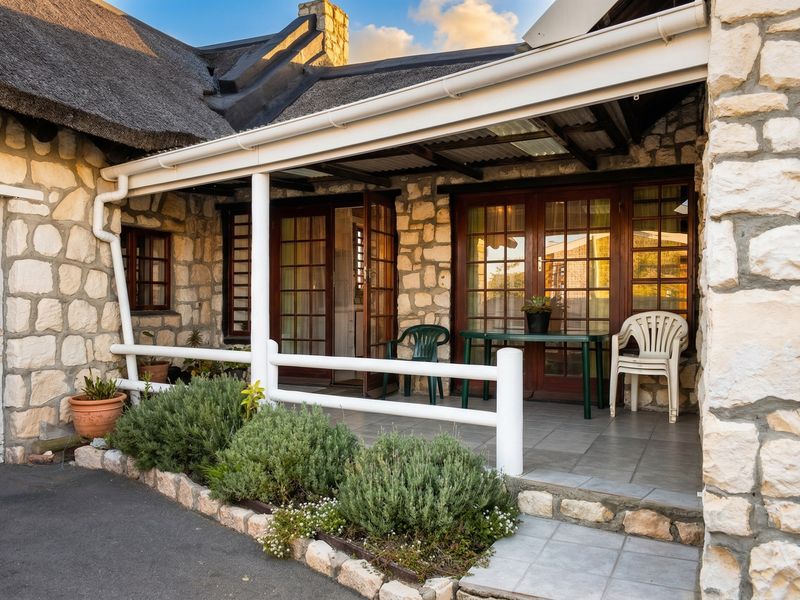 A covered patio area featuring stone cladding, a thatched roof, and timber-framed glass doors providing access to the interior.