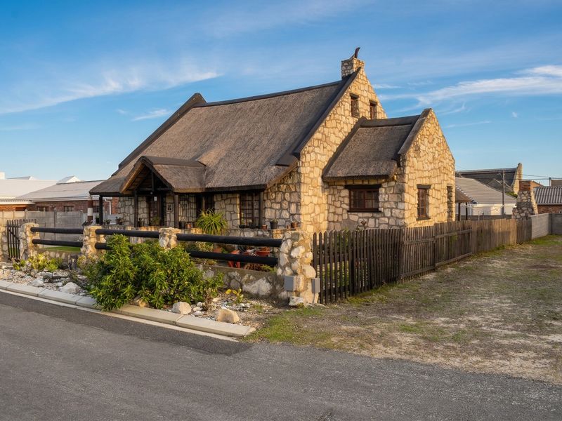 A charming stone-clad cottage featuring a traditional thatched roof, timber fencing, and a well-defined front garden area.