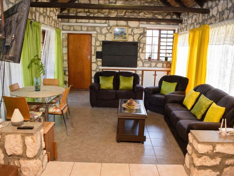 Open-plan living and dining area featuring rustic stone masonry walls, exposed timber ceiling beams, tiled flooring, and a built-in fireplace.