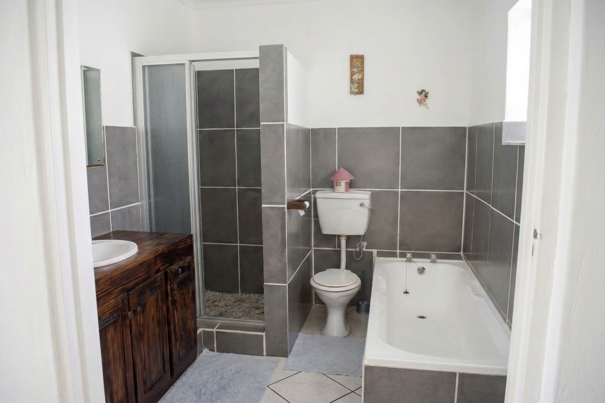 A functional bathroom featuring a shower enclosure, bathtub, toilet, and a wooden vanity with a basin, finished with grey wall tiles.