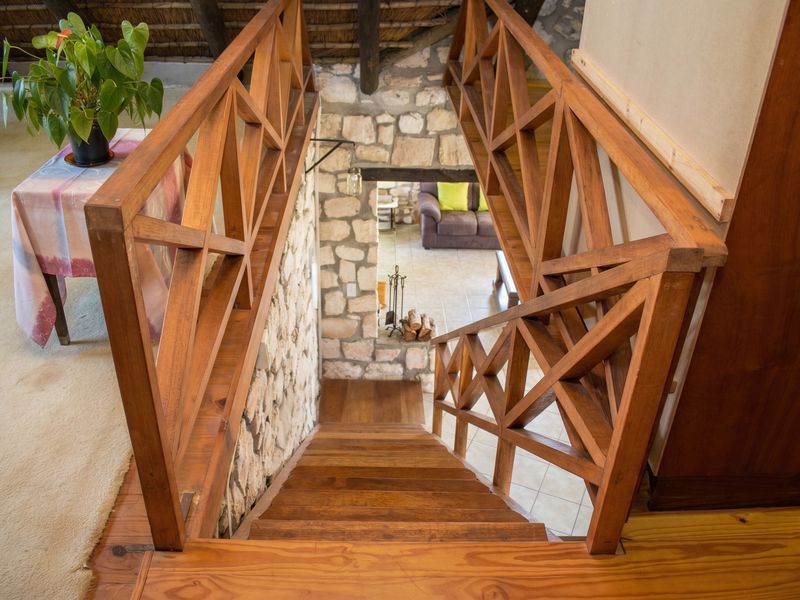 A wooden staircase with a decorative balustrade leading down, featuring rustic stone wall accents and a visible thatched roof structure above.
