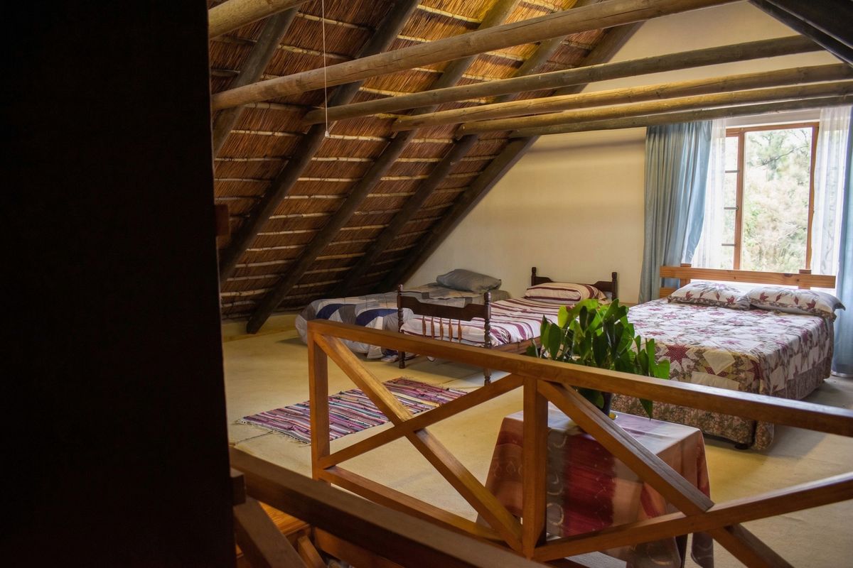 Spacious loft-style bedroom featuring exposed timber rafters, a traditional thatched roof, and a wooden balustrade overlooking the lower level.