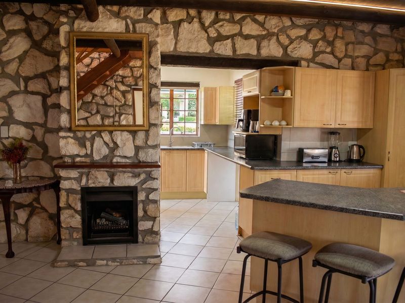 Open plan living area featuring a rustic stone fireplace and a functional kitchen with light wood cabinetry and tiled flooring.
