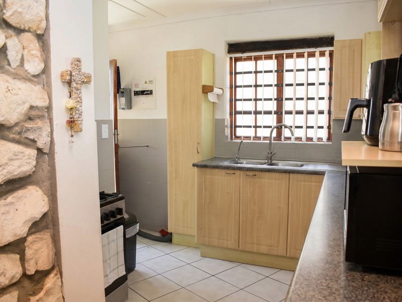 Functional kitchen featuring light wood-finish cabinetry, a double basin sink, tiled splashbacks, and a distinctive stone feature wall.